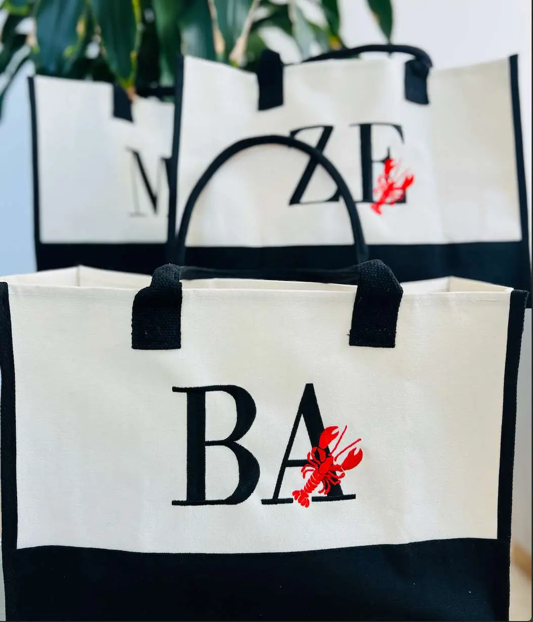 Tote bags blancos con iniciales en negro y una langosta roja bordada